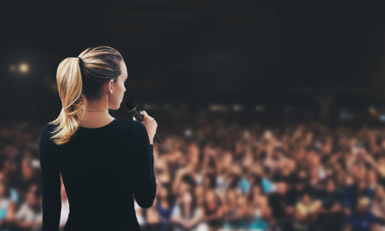 Mobile image of a female speaking to a crowd using a microphone
